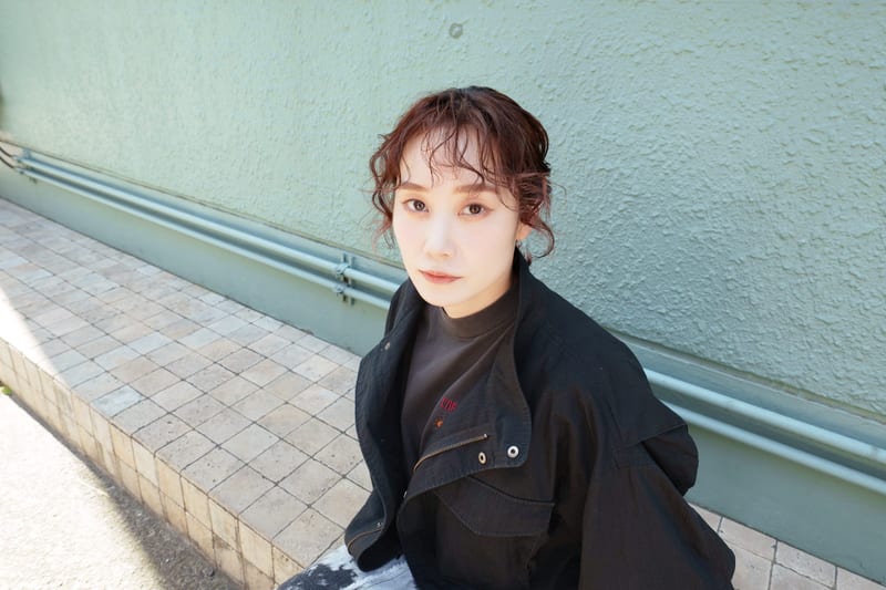 Sitting on a tiled ledge against a pale green wall, a person looks up at the camera