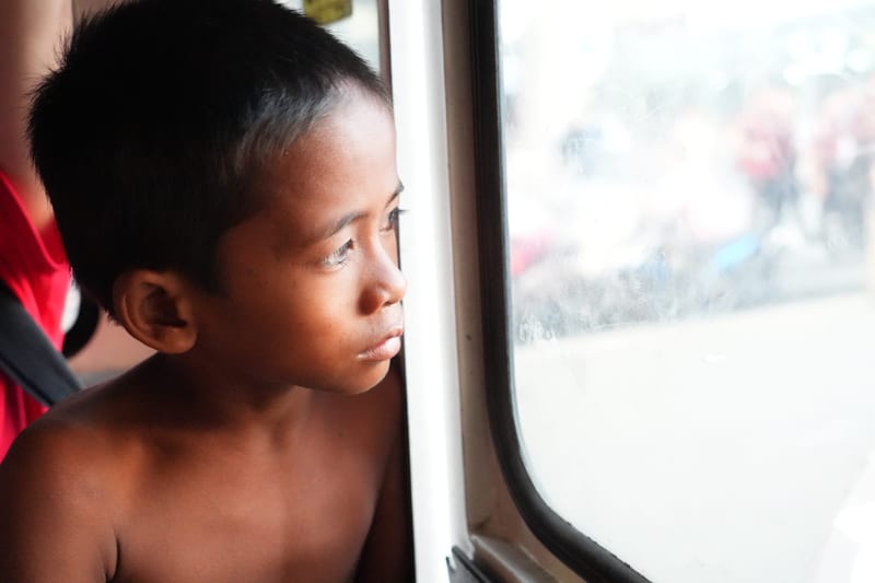 A boy looks out through the window of a jeepney, sunlight on his face