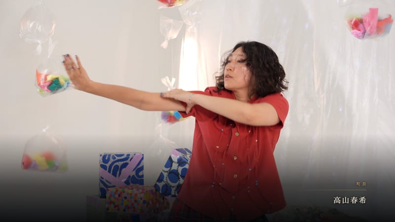 A dancer in a red shirt stretches her arms out in front of floating paper decorations