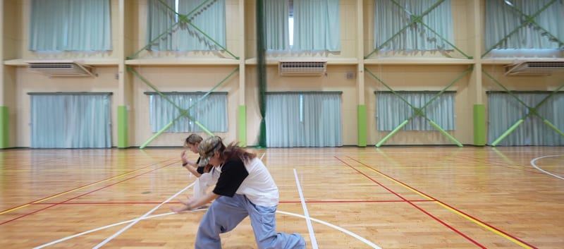 Two dancers move low across the floor of a school gym