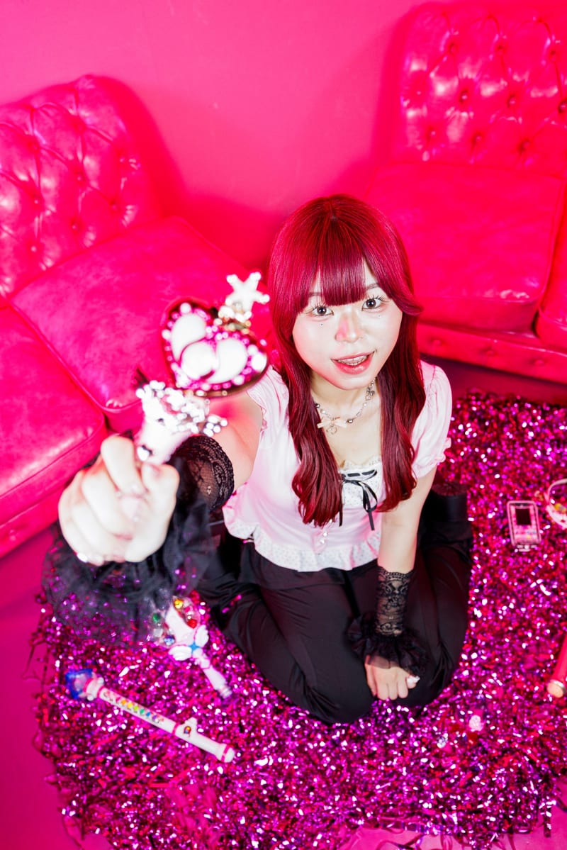A person with red hair sits on the floor of a hot pink room and looks up at the camera