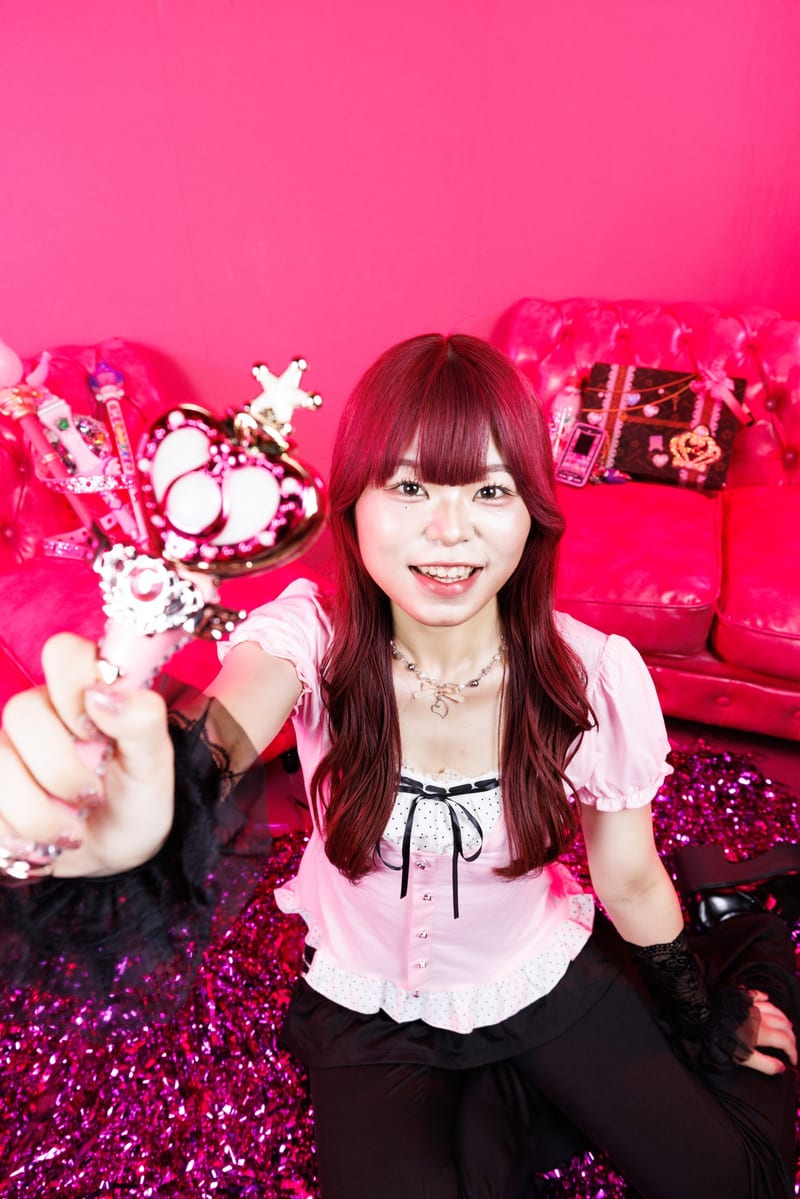 Close to the camera, a person in a pink blouse holds out a heart wand and laughs