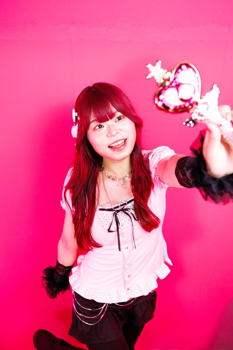 Against a hot pink wall, a person laughs and stretches a heart wand out of the frame