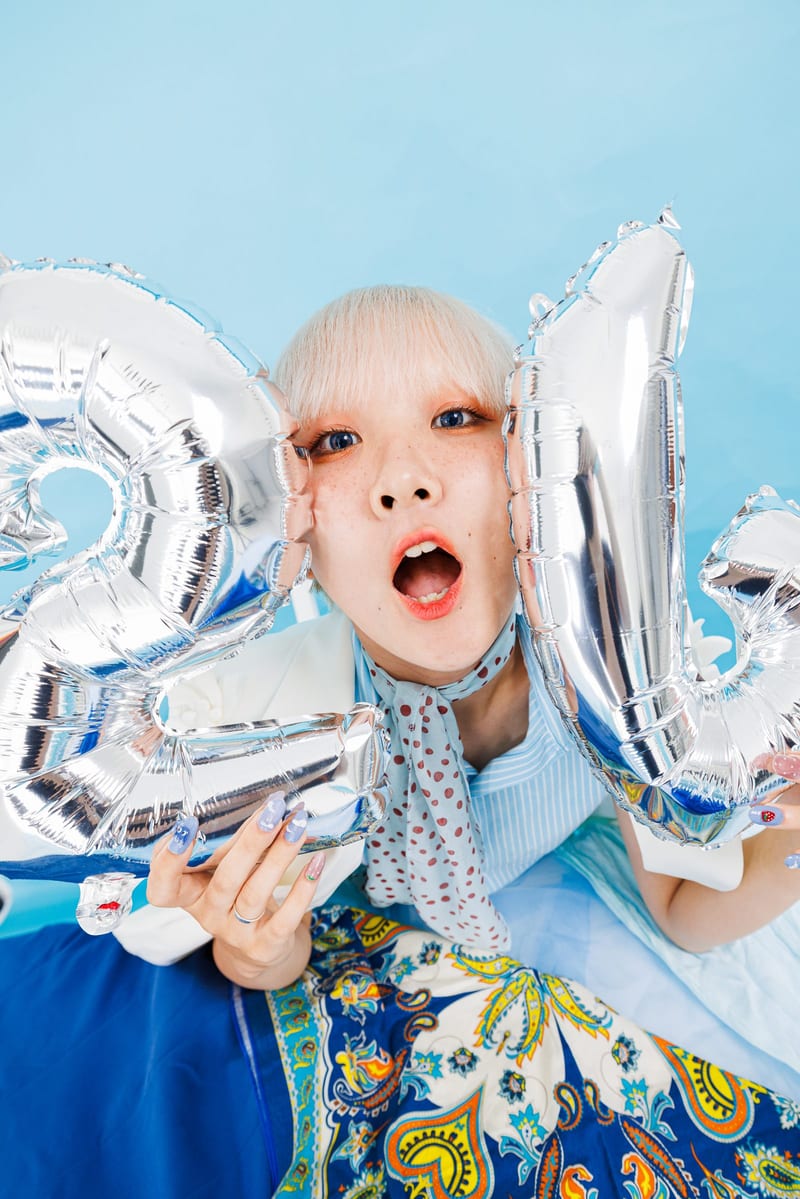 Holding two silver balloons, a person opens their mouth wide toward the camera