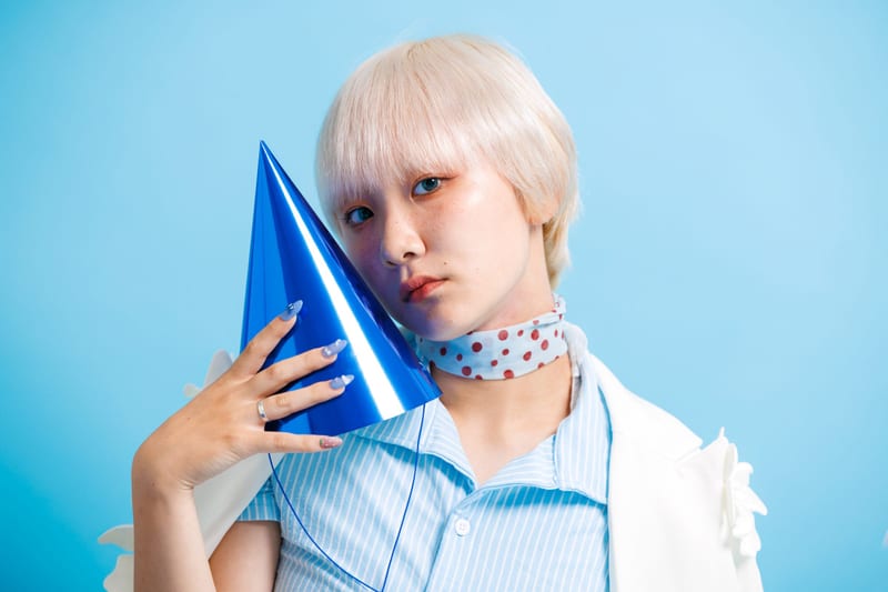 Close up, a person holds a shiny blue cone hat against their cheek