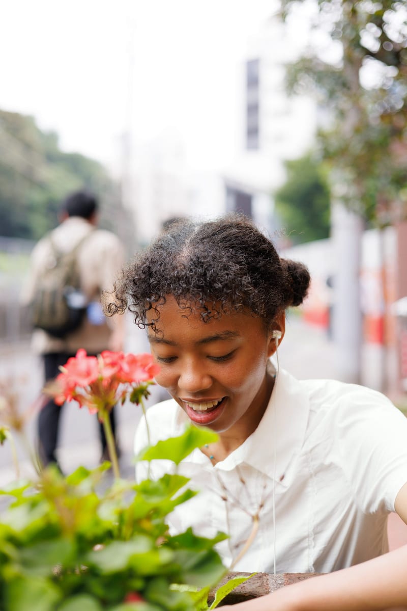 On a city pavement, a person in a white shirt smiles down at pink flowers