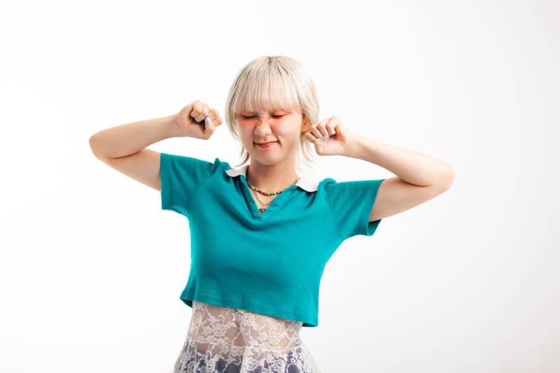 Eyes squeezed shut, a person in a teal shirt holds their fists up beside their head