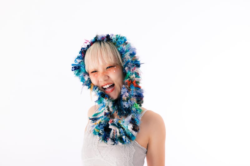 Laughing with eyes closed, a person in a hood of blue and green yarn