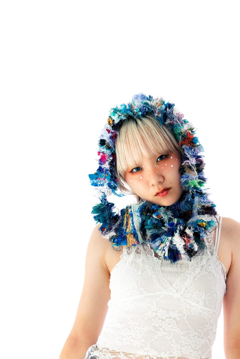 In a knitted hood and a white lace top, a person looks into the camera