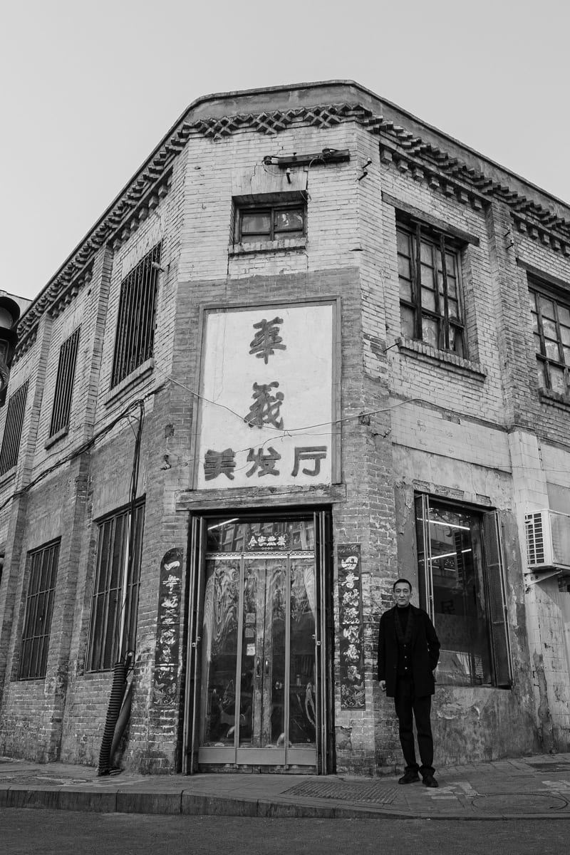 Black and white: an old corner building with a barbershop sign, a man standing at its door
