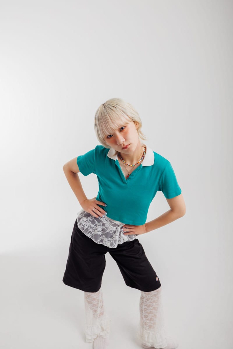 Leaning forward with hands on hips, a person in a teal shirt, black shorts and white lace socks