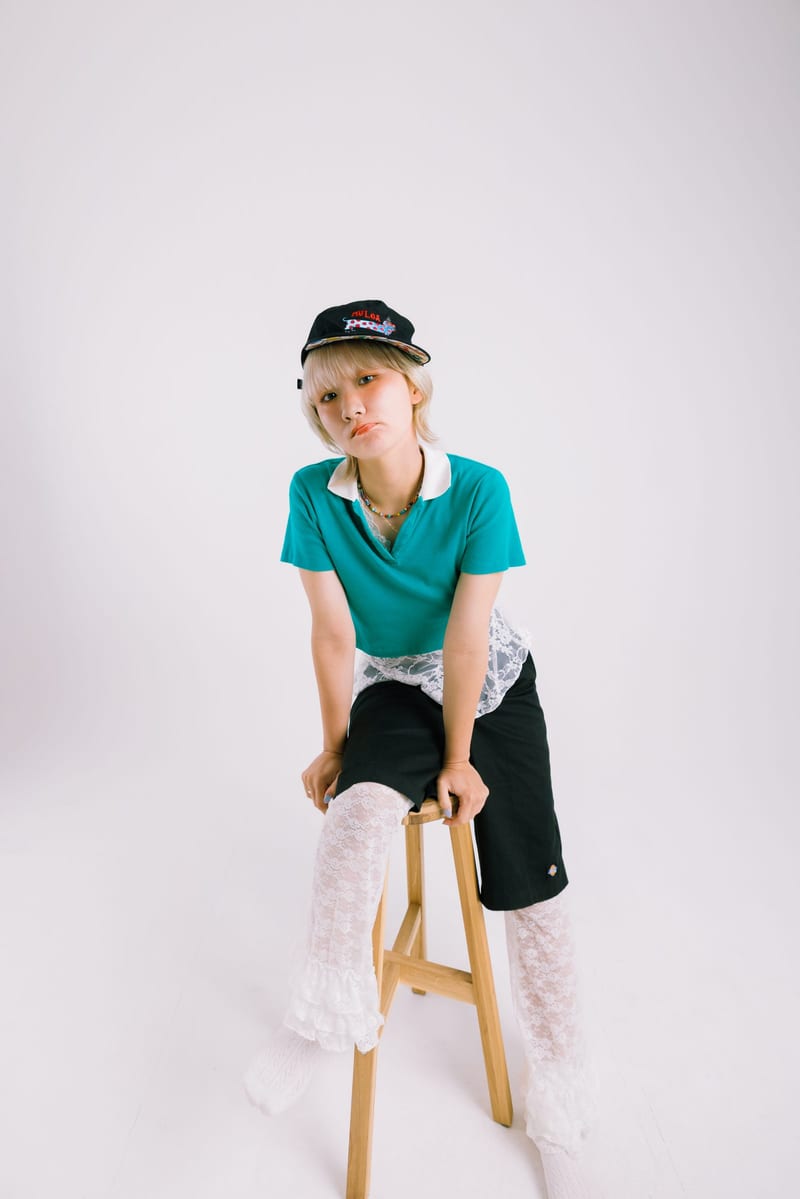 Perched on a tall wooden stool, a person in a teal shirt and lace socks against a white backdrop