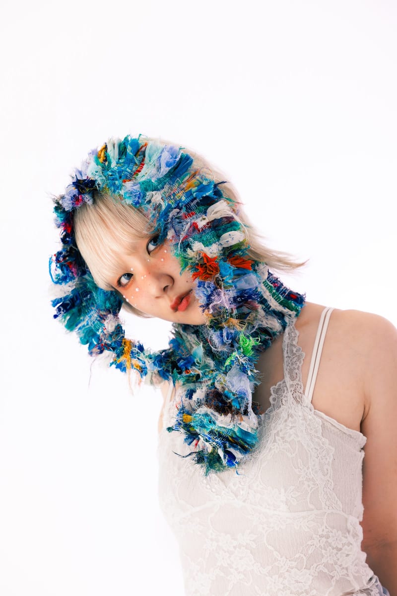 Against a white background, a person wears a hood knitted from blue, white and green yarn