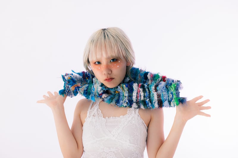A long knitted scarf of blue and green yarn wrapped around a person's neck, hands raised at their sides