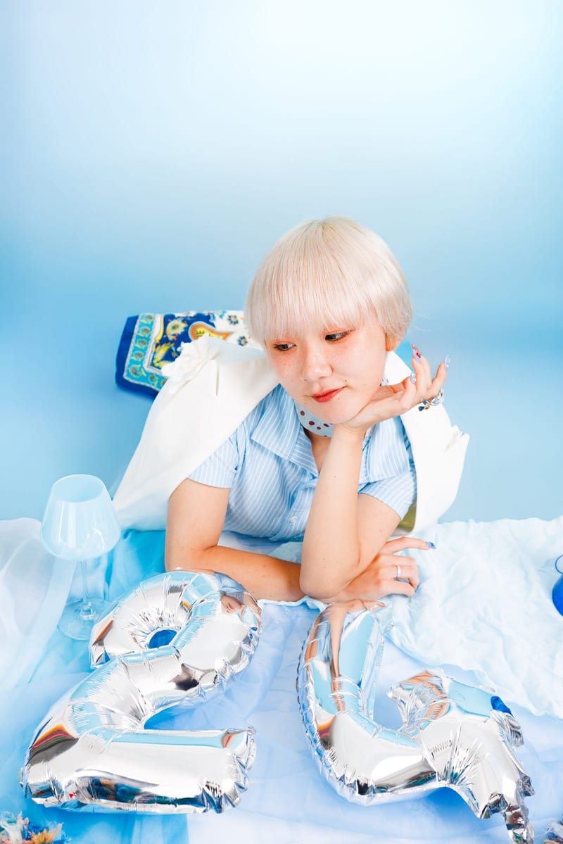 The same pose from further back, the balloons and pale blue cloth filling the foreground