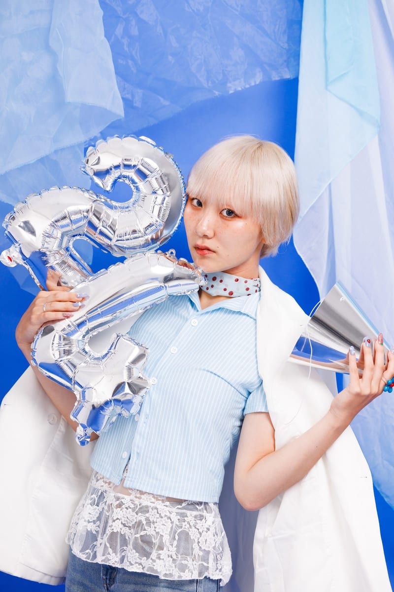Standing among sheer curtains, a person hugs silver number balloons